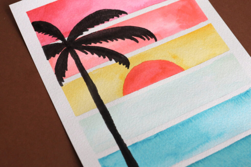 Image contains a close up view of the silhouette of a palm tree drawn on top of a watercolor sunset.