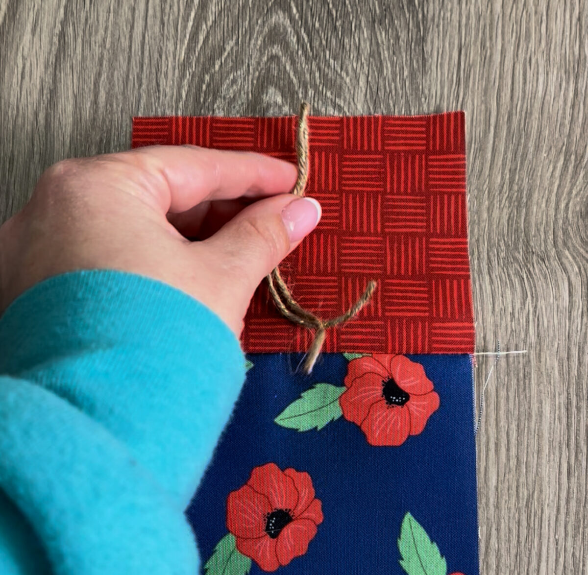 Image contains Amy’s hand holding a piece of twine and placing it on the top of the fabric firecracker.