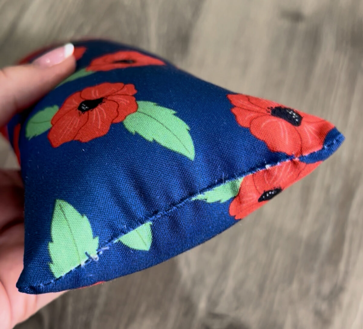Image is a close up of the bottom of a fabric firecracker, hand stitched shut.