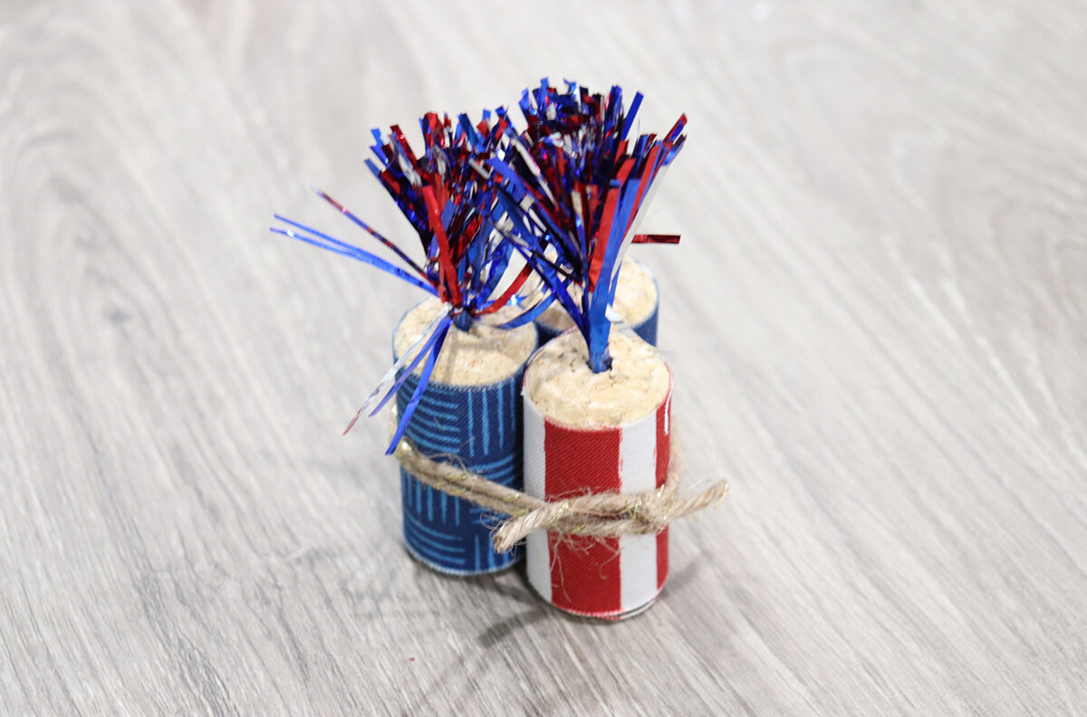 Image contains three cork firecrackers tied together with a piece of twine, sitting on a wooden table.