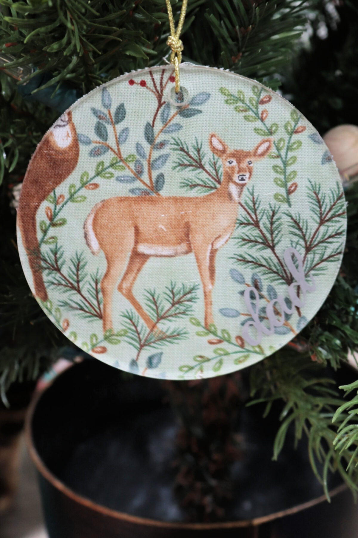 Image contains a round ornament with a green background and a brown deer in the center.