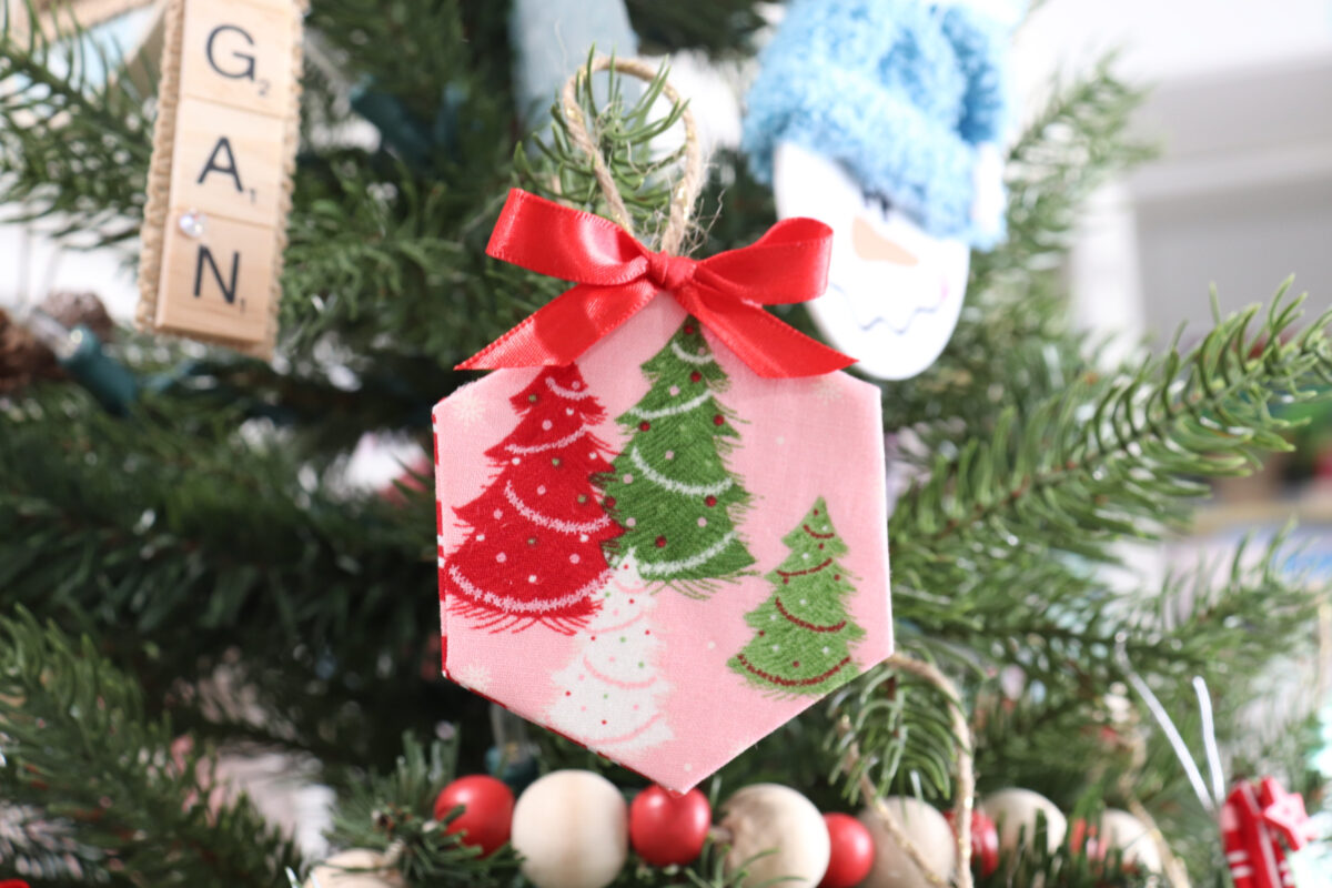 Image contains a fabric wrapped hexagon ornament featuring pink fabric with red, white, and green trees. 