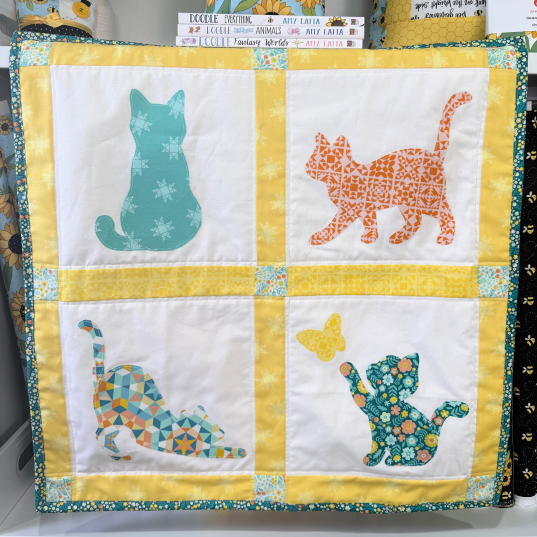 Image contains a quilted wall hanging featuring four different cat silhouette shapes.