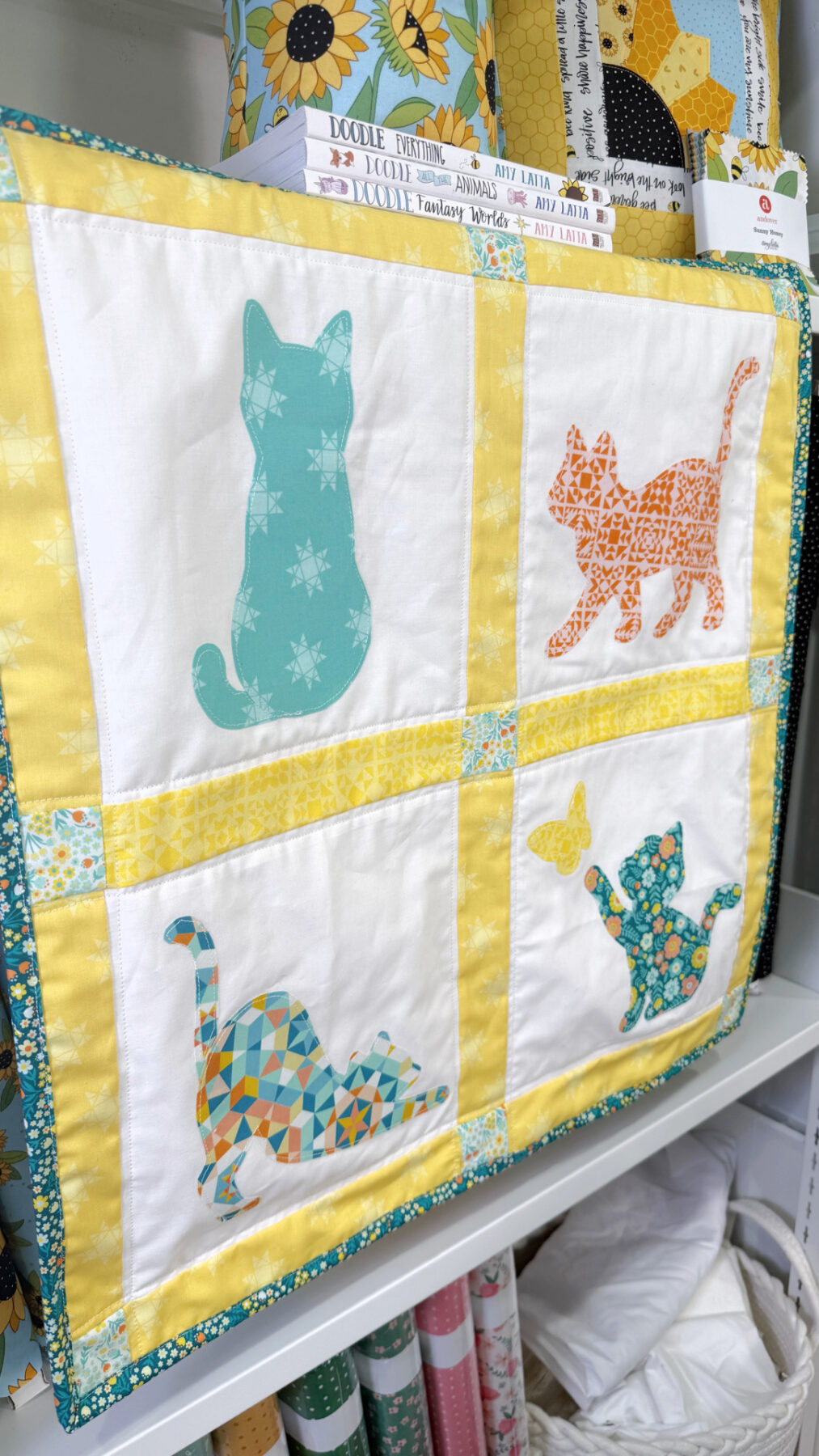 Image contains a quilted wall hanging featuring four applique cat shapes.